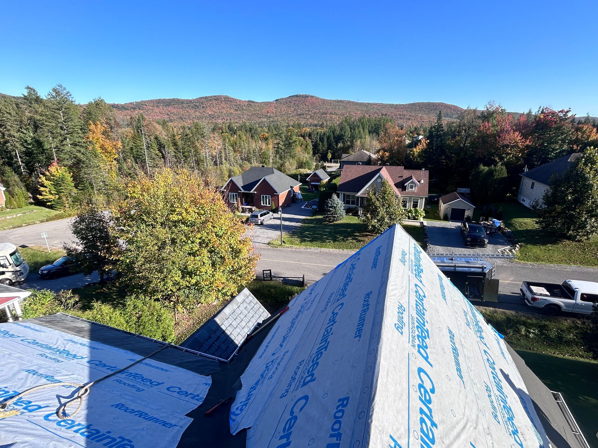 Vue depuis le toit d'un quartier avec des arbres et des maisons, ciel bleu, toit en construction.