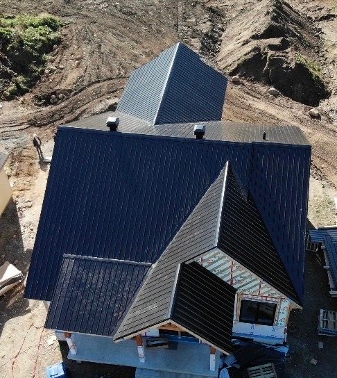 Toiture métallique sombre sur une maison en construction. De la terre brune entoure la structure.