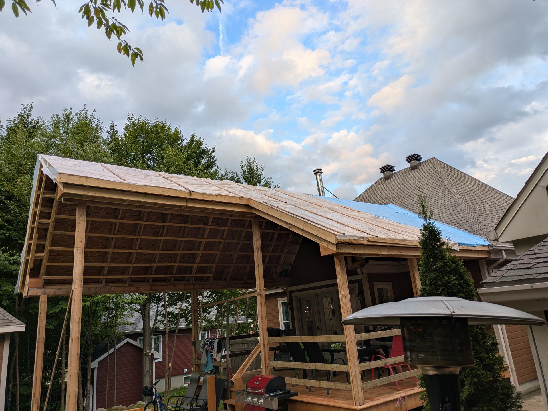 Terrasse en bois avec un toit neuf, bâche bleue et ciel nuageux.