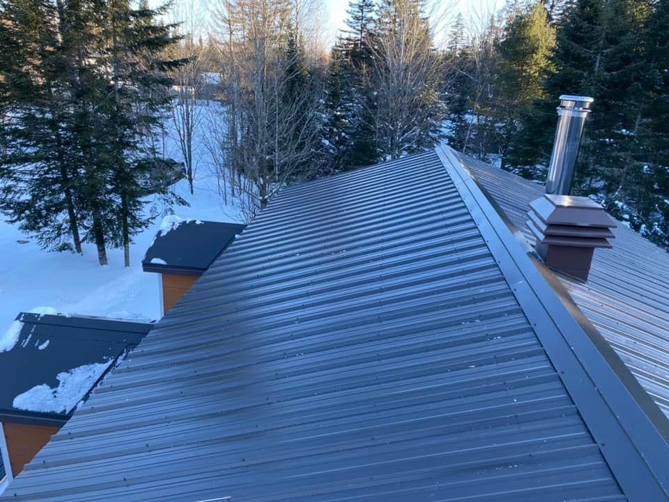 Toit métallique sur un bâtiment enneigé avec des arbres en arrière-plan.