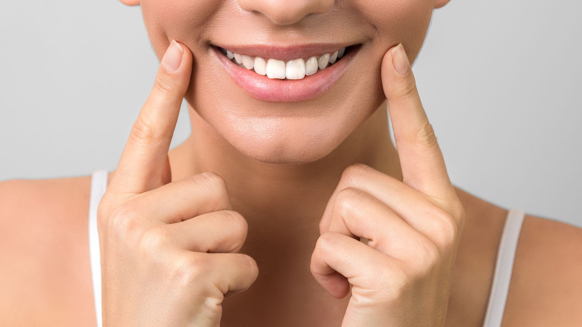 Close-up of a smiling woman with white teeth, with her fingers pointed on each cheek. Close-up of a smiling woman with white teeth, with her fingers pointed on each cheek.