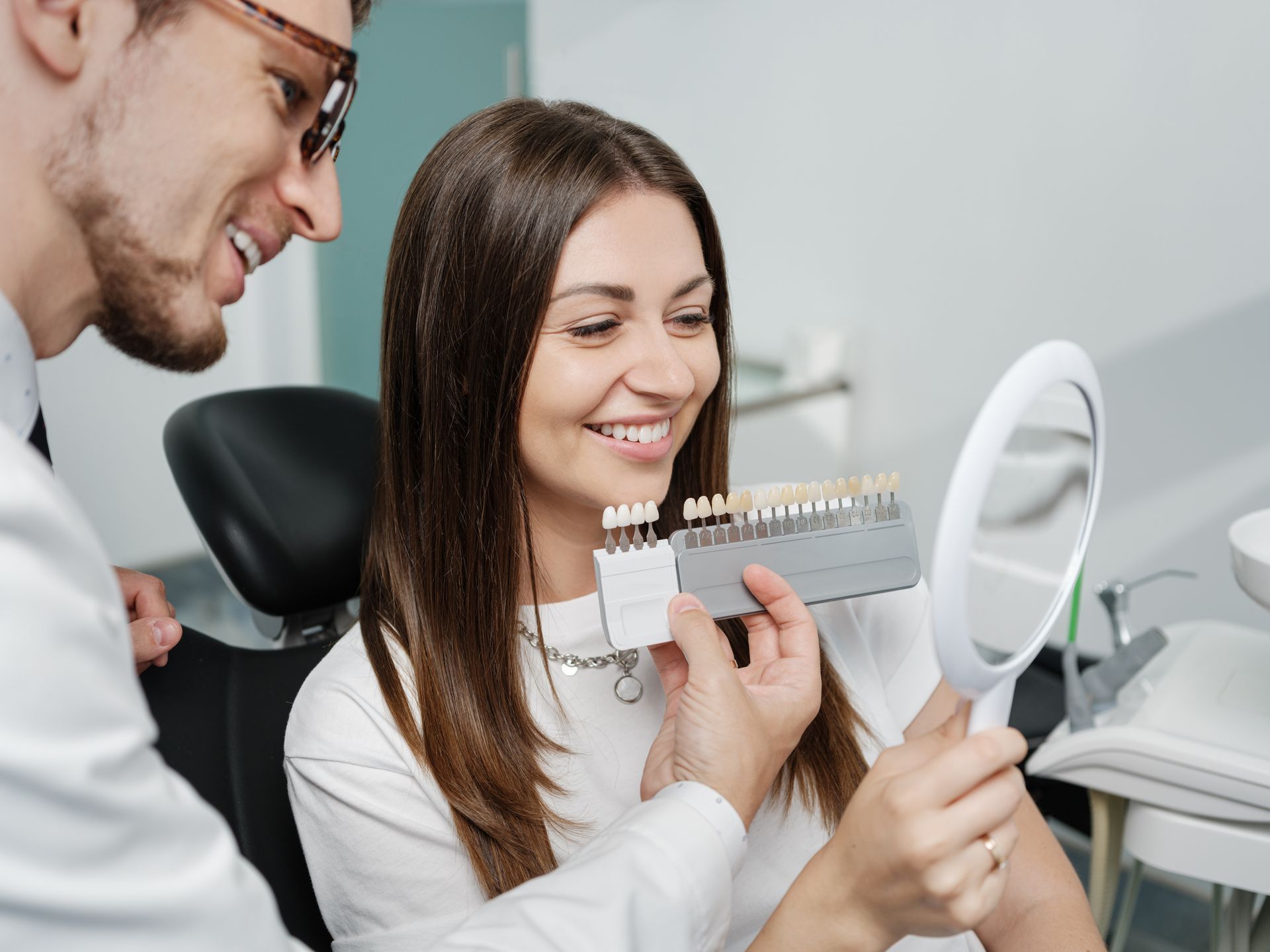A dentist shows a veneer enamel colour palette to a patient as she looks at a mirror.