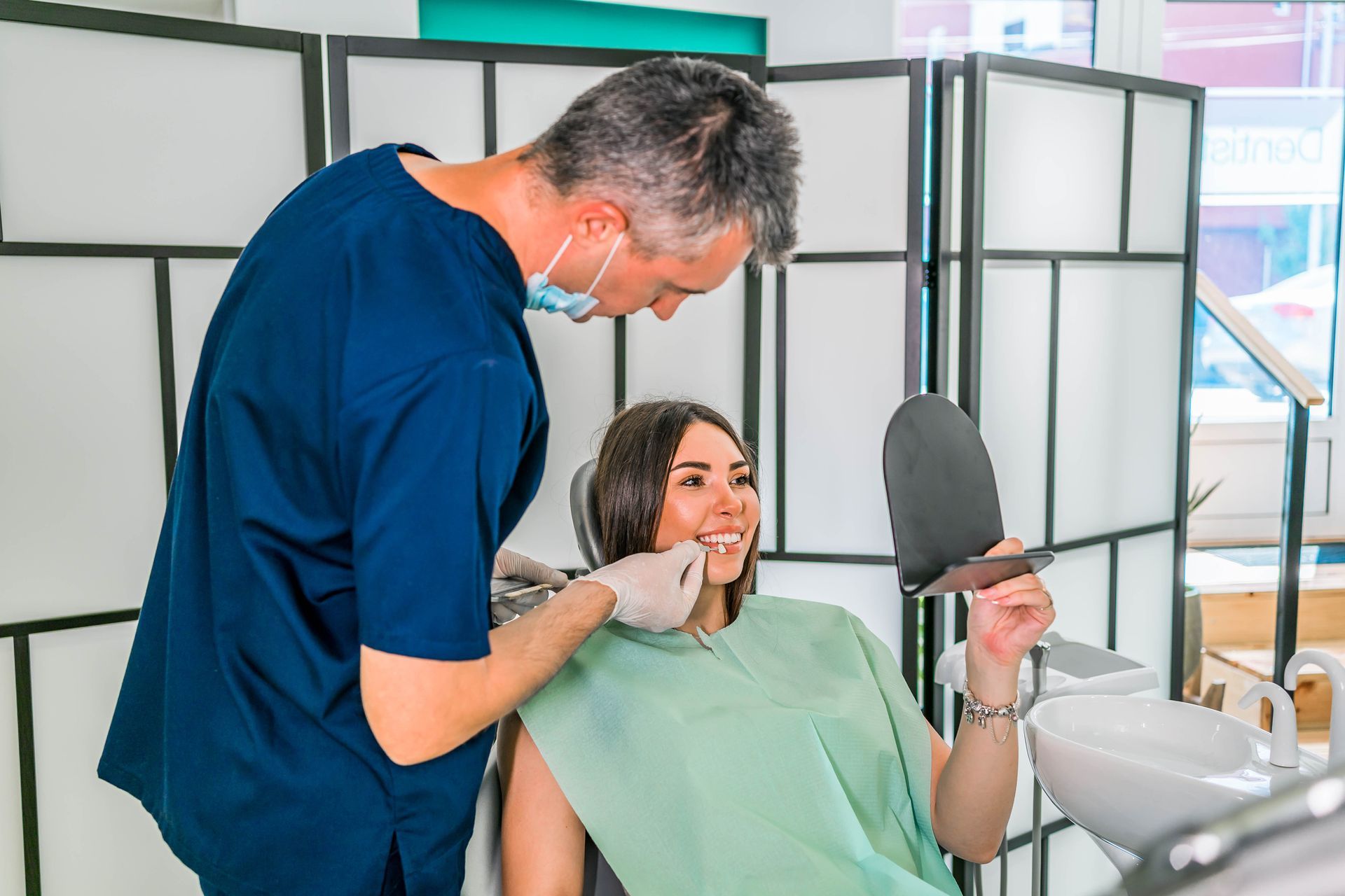 patient in chair smiling at mirror while dentist examines her teeth.