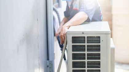 A man is fixing an air conditioner on the side of a building.
