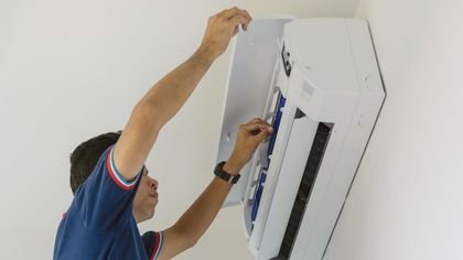 A man is fixing an air conditioner on the wall.