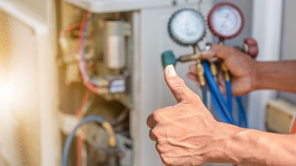 A man is giving a thumbs up while working on an air conditioner.