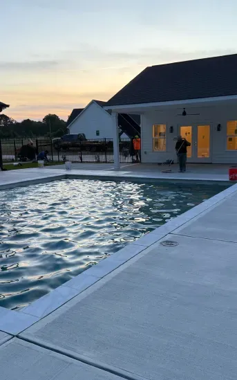 Poolside patio at dusk beside a lit building and calm water.