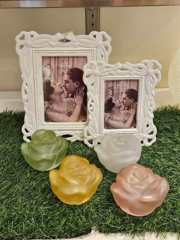 Due cornici decorative bianche con foto e quattro portacandele colorati a forma di rosa su un prato verde.