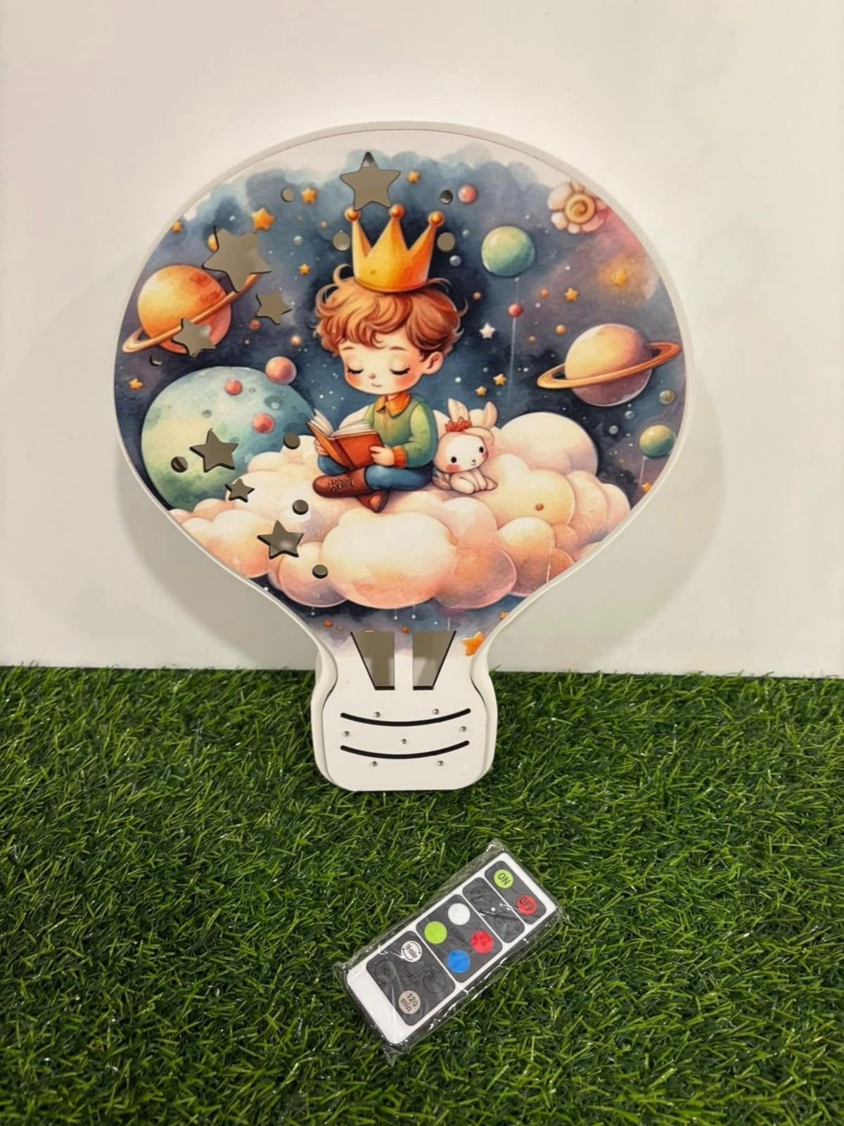 Luce notturna a forma di lampadina con scena spaziale e un ragazzo che legge, con telecomando sull'erba.