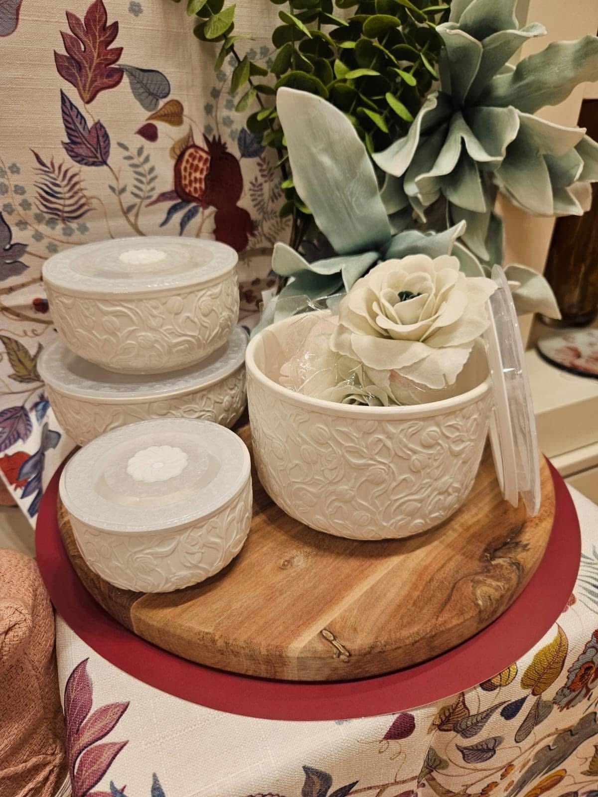 Ciotole in ceramica bianca con motivo floreale su un vassoio di legno con fiori finti.
