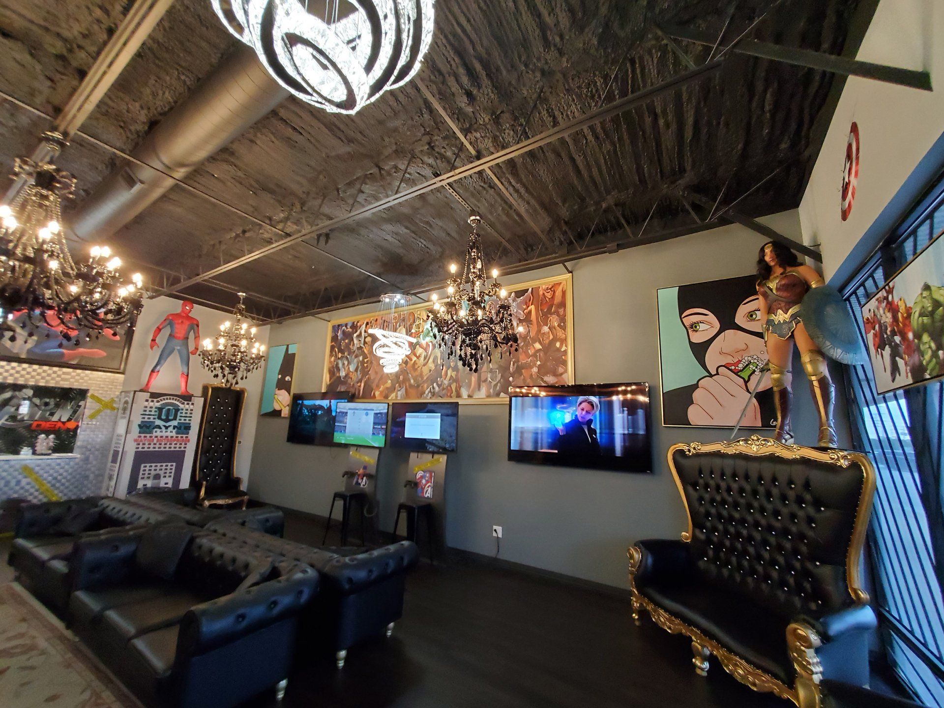 Modern lounge with black leather couches, wall-mounted TVs, and a gold-trimmed throne chair under a high ceiling.