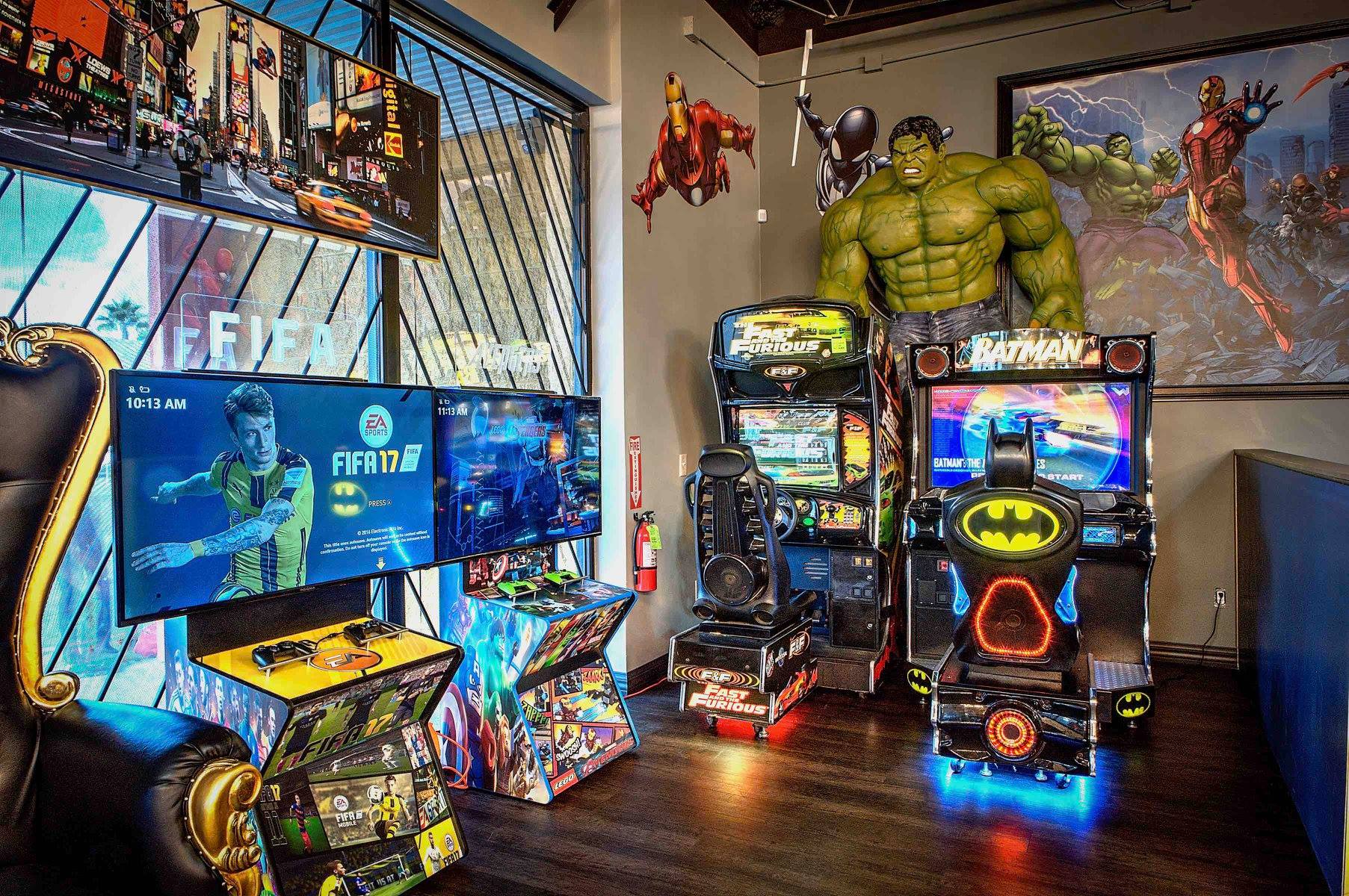 Colorful game room with multiple screens, arcade cabinets, and a large Hulk figure on display