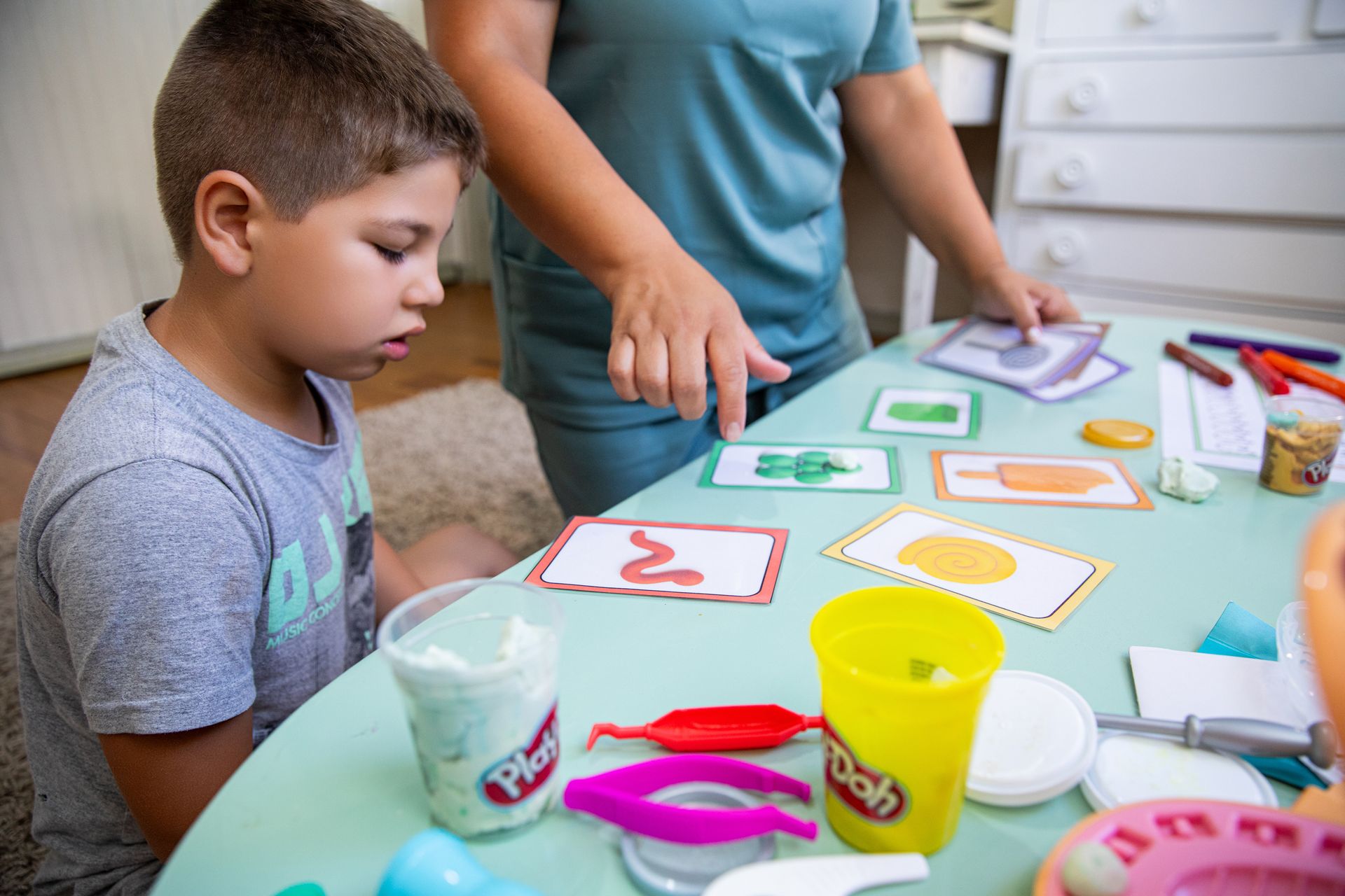 Criança observa adulto organizar cartões coloridos com formas geométricas sobre uma mesa