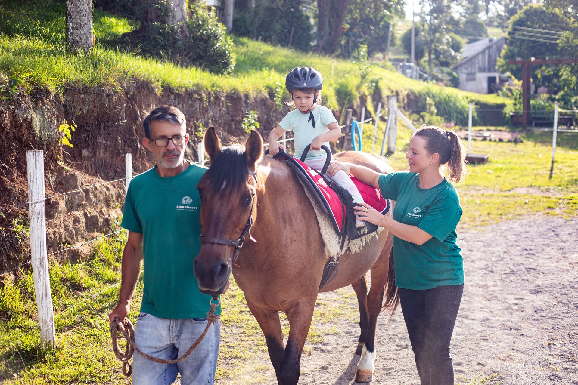 Um adulto e uma criança montando um cavalo marrom ao ar livre, com duas pessoas caminhando