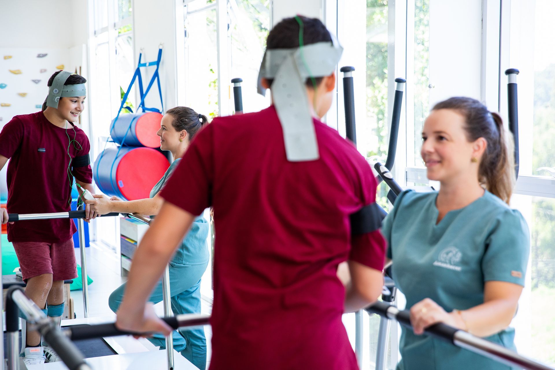 Pessoas se exercitando em barras paralelas em uma academia de fisioterapia bem iluminada.