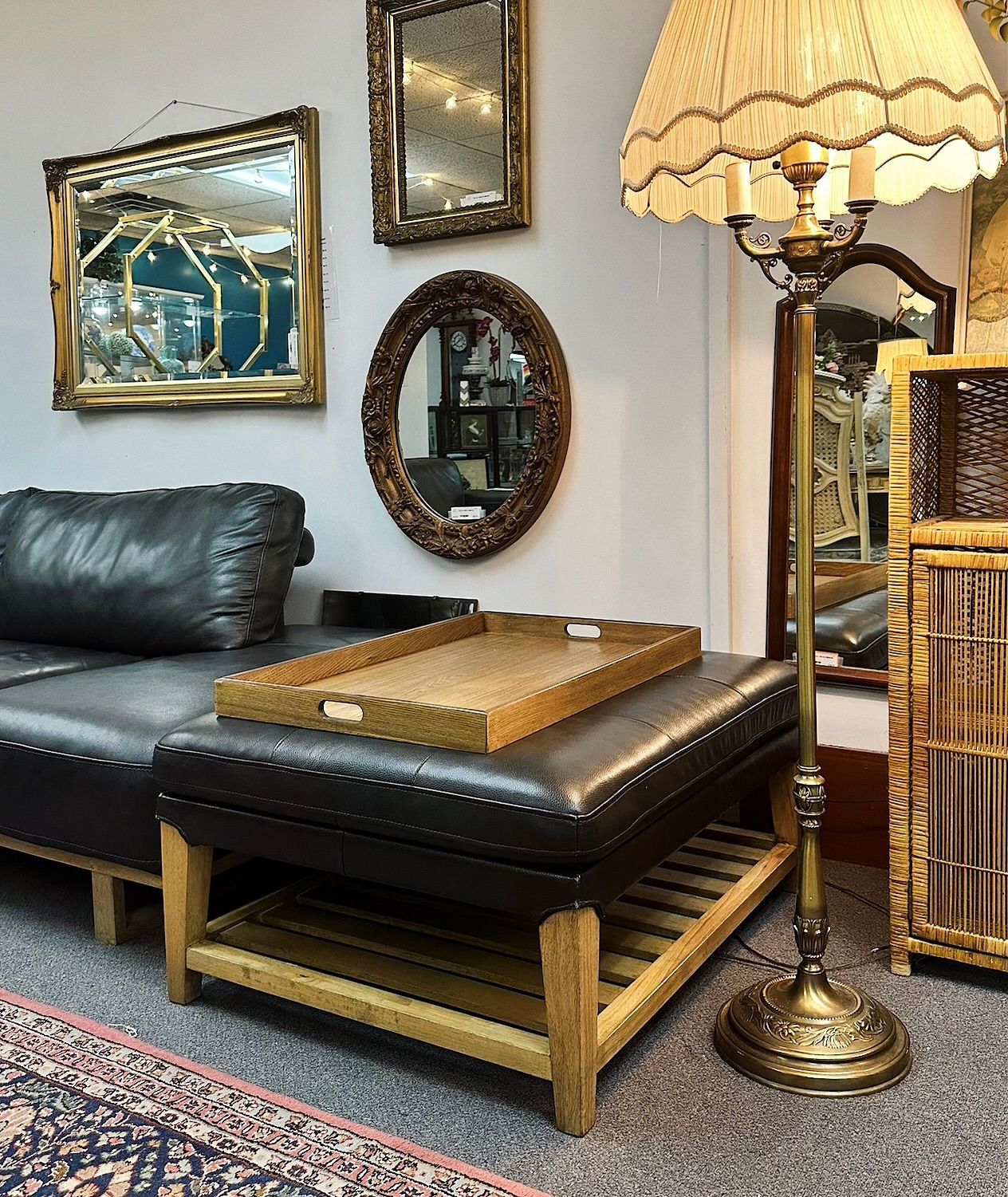 Cozy living room corner with black leather ottoman, gold floor lamp, wall mirrors, and framed art