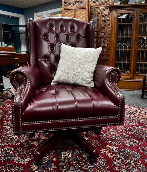 Burgundy leather tufted armchair with a white cushion on a patterned rug in an antique-furnished room