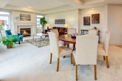 Bright living and dining room with fireplace, beige carpet, white chairs, and wooden table