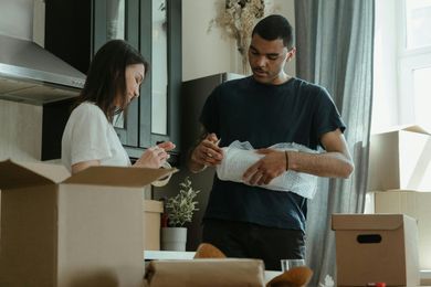 Two people unpacking items in a kitchen, with open boxes and packing materials on the counter.