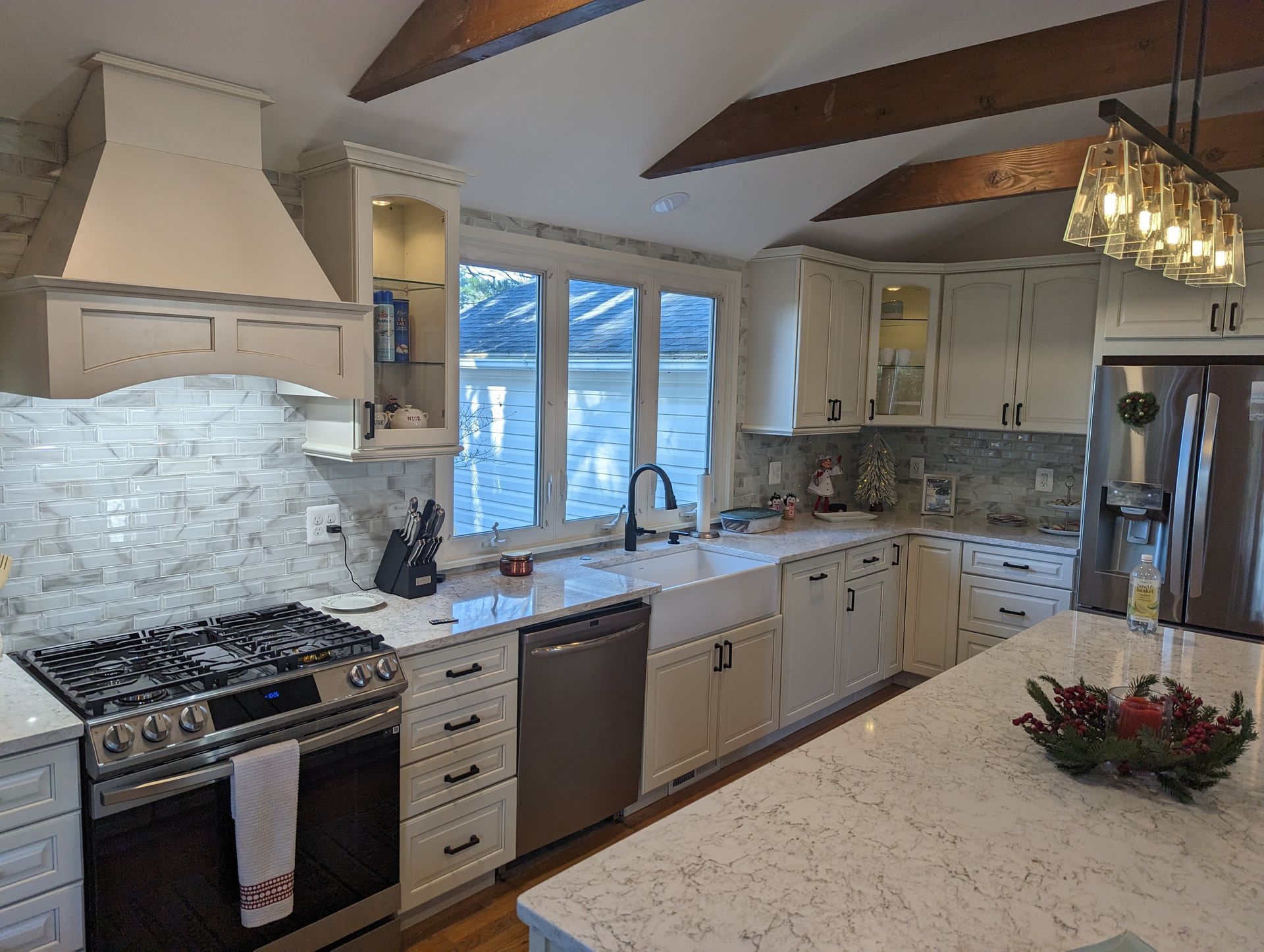 A bright, renovated kitchen with white cabinets, marble backsplash, stainless steel appliances, and an island with a festive centerpiece.