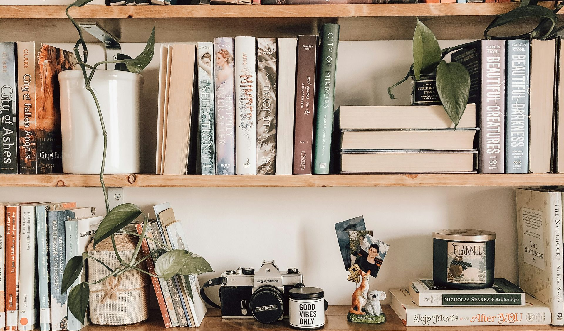 Hands arranging books on a shelf, lit by warm light, with papers and a pen visible.
