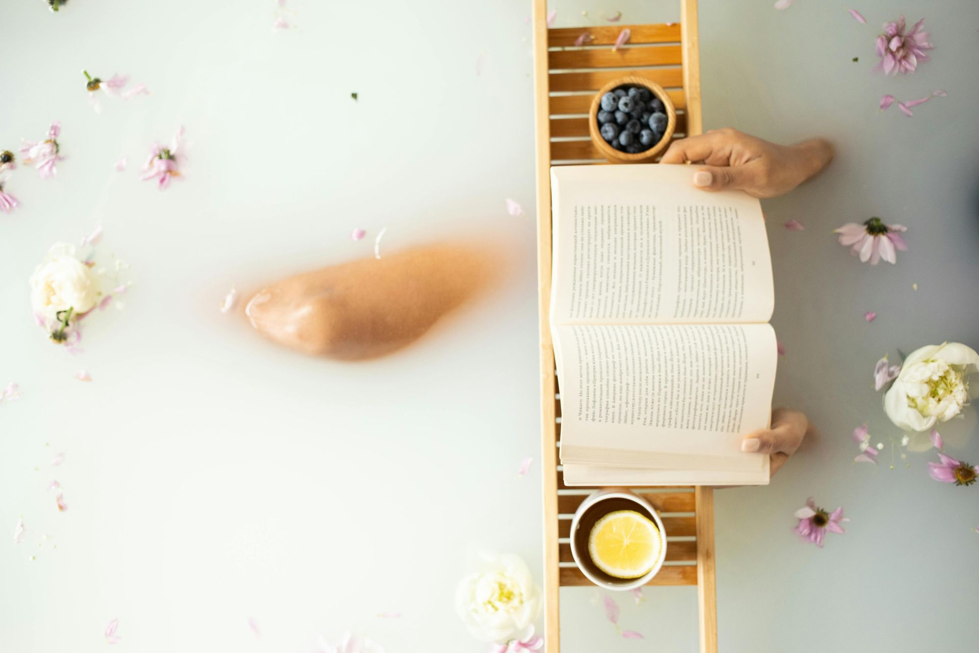Feet with red toenails in a bubbly bathtub, a book resting nearby.