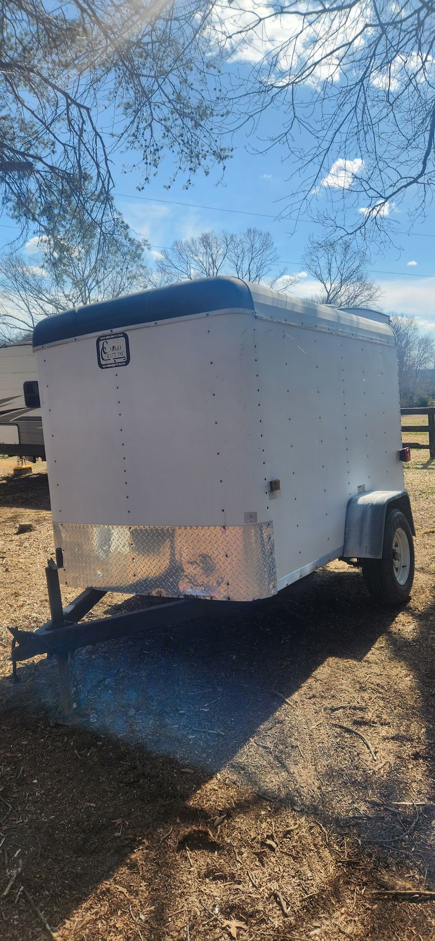 A white trailer is parked in a field next to a tree.