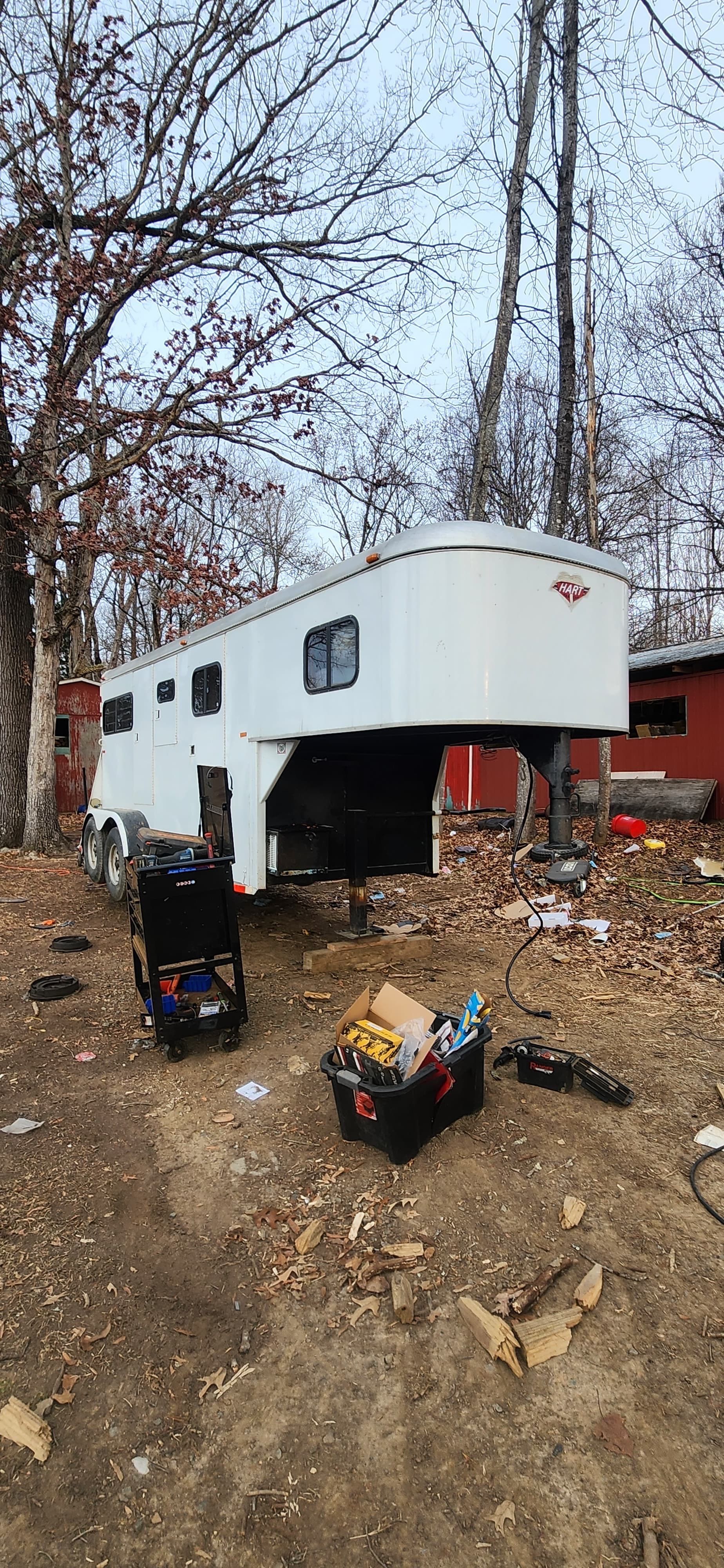 White horse trailer on gravel driveway, surrounded by trees.