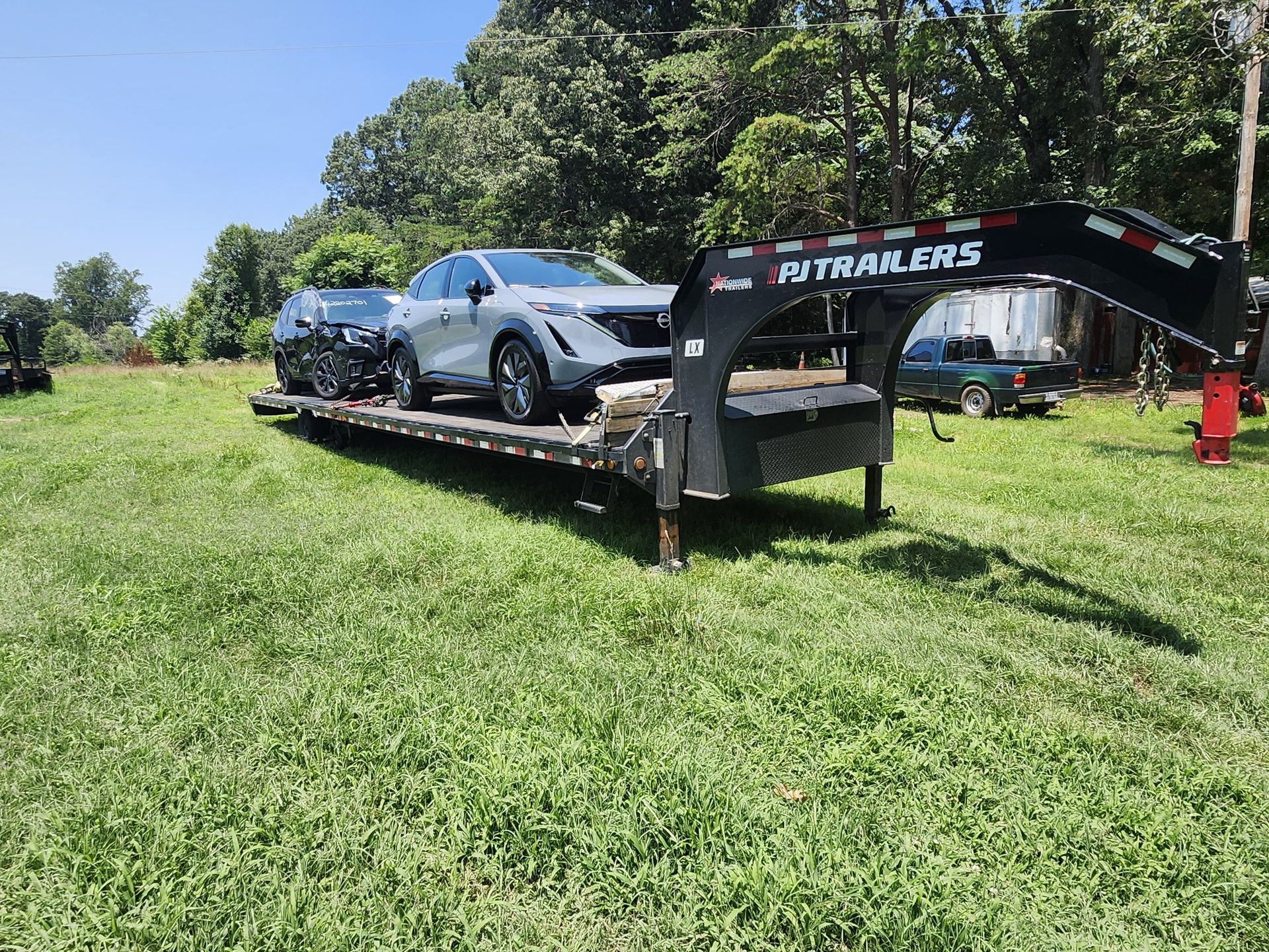 Black utility trailer on grass, red barn in background.