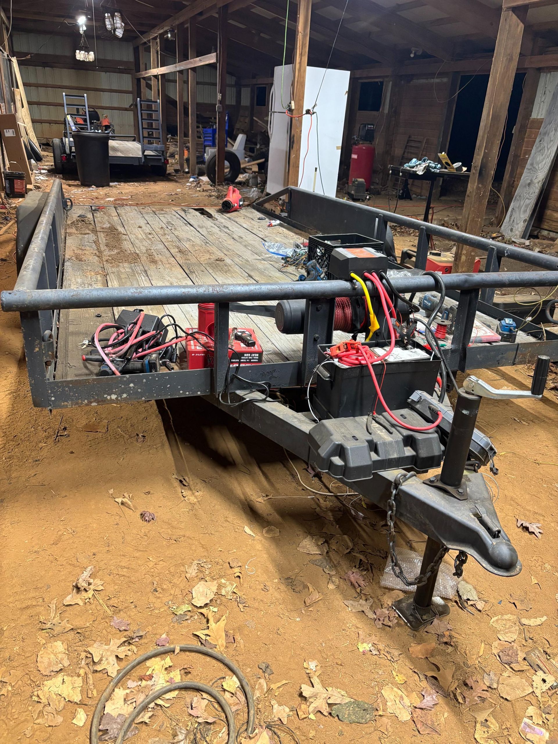 Black utility trailer with engine and wiring in a rustic barn setting.