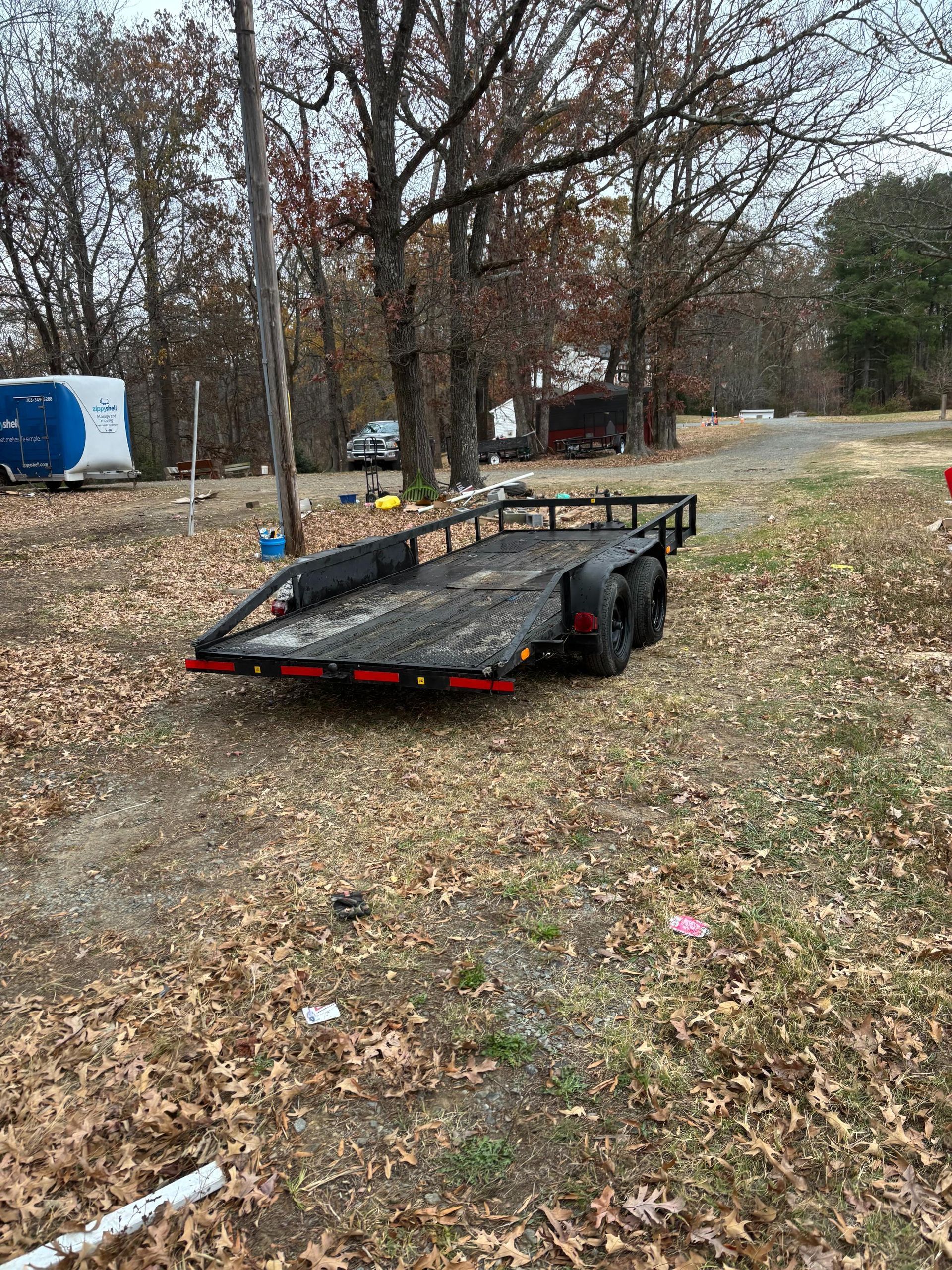 Trailer parked on a dirt lot. Trees and a small building in the background. Overcast day.