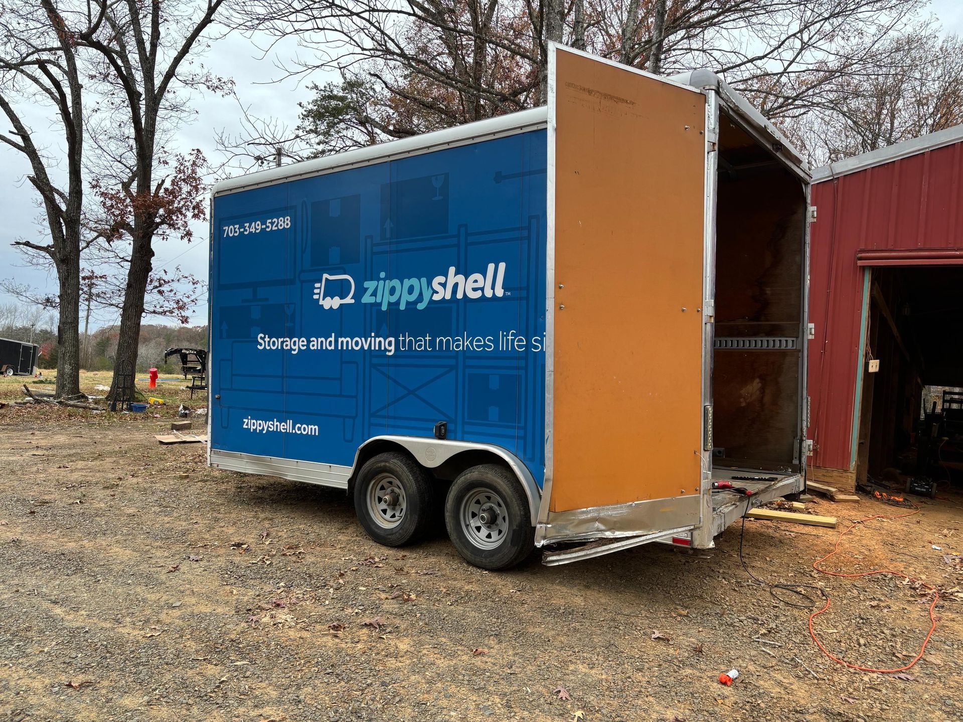 Blue and orange Zippy Shell storage trailer with open back door, parked outside a building.