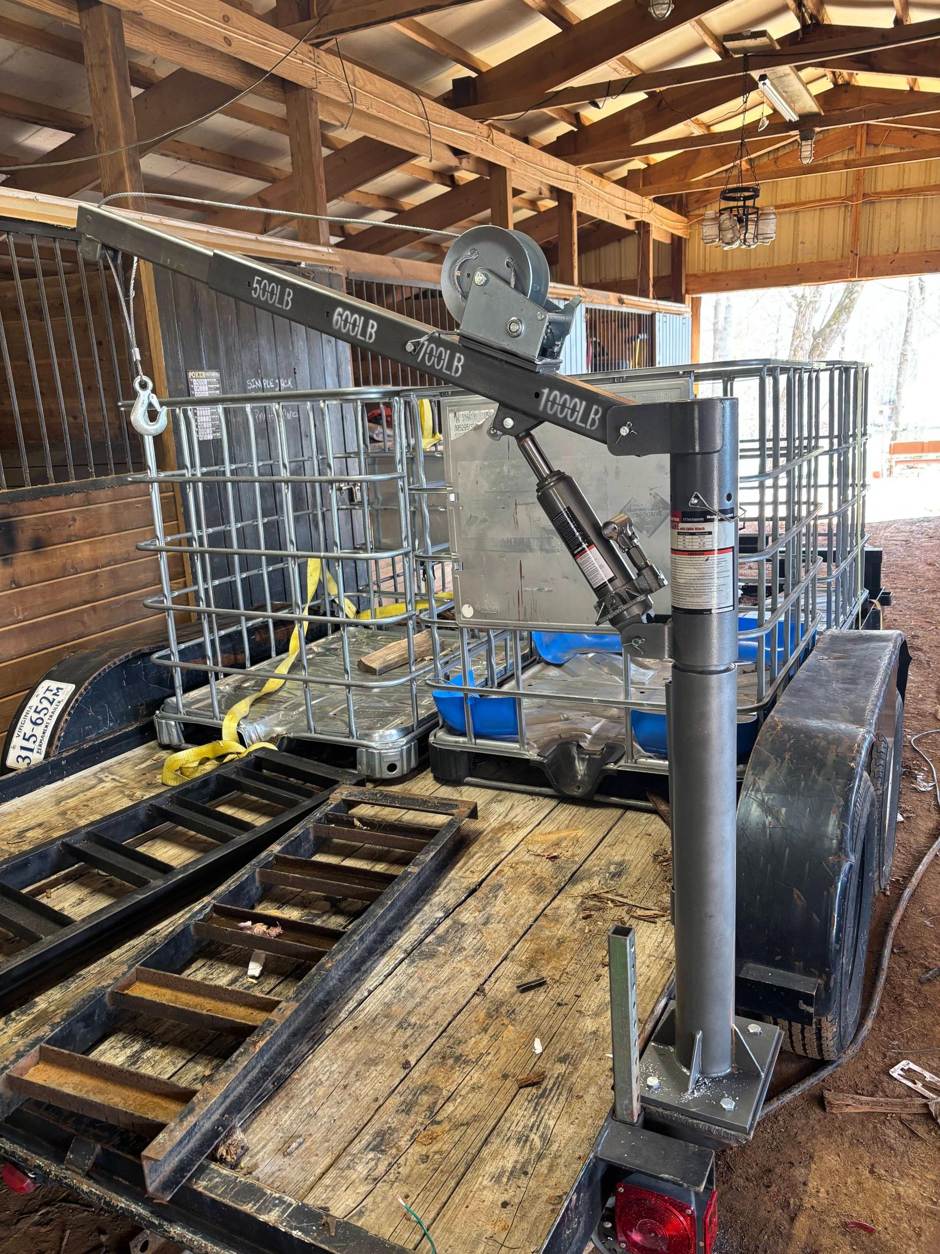 A truck-mounted utility crane installed on a wooden trailer bed near industrial containers inside a barn.