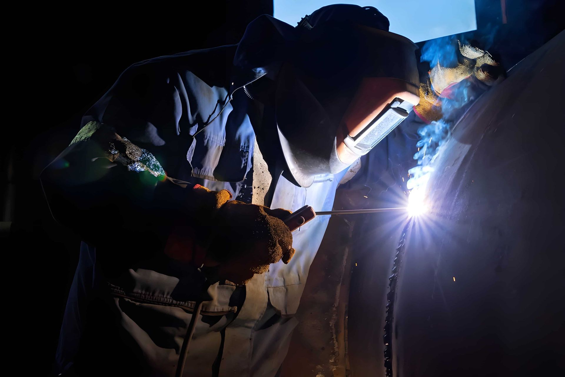 A Man Is Welding a Piece of Metal in A Dark Room — Betts Welding Pty Ltd In Moss Vale, NSW