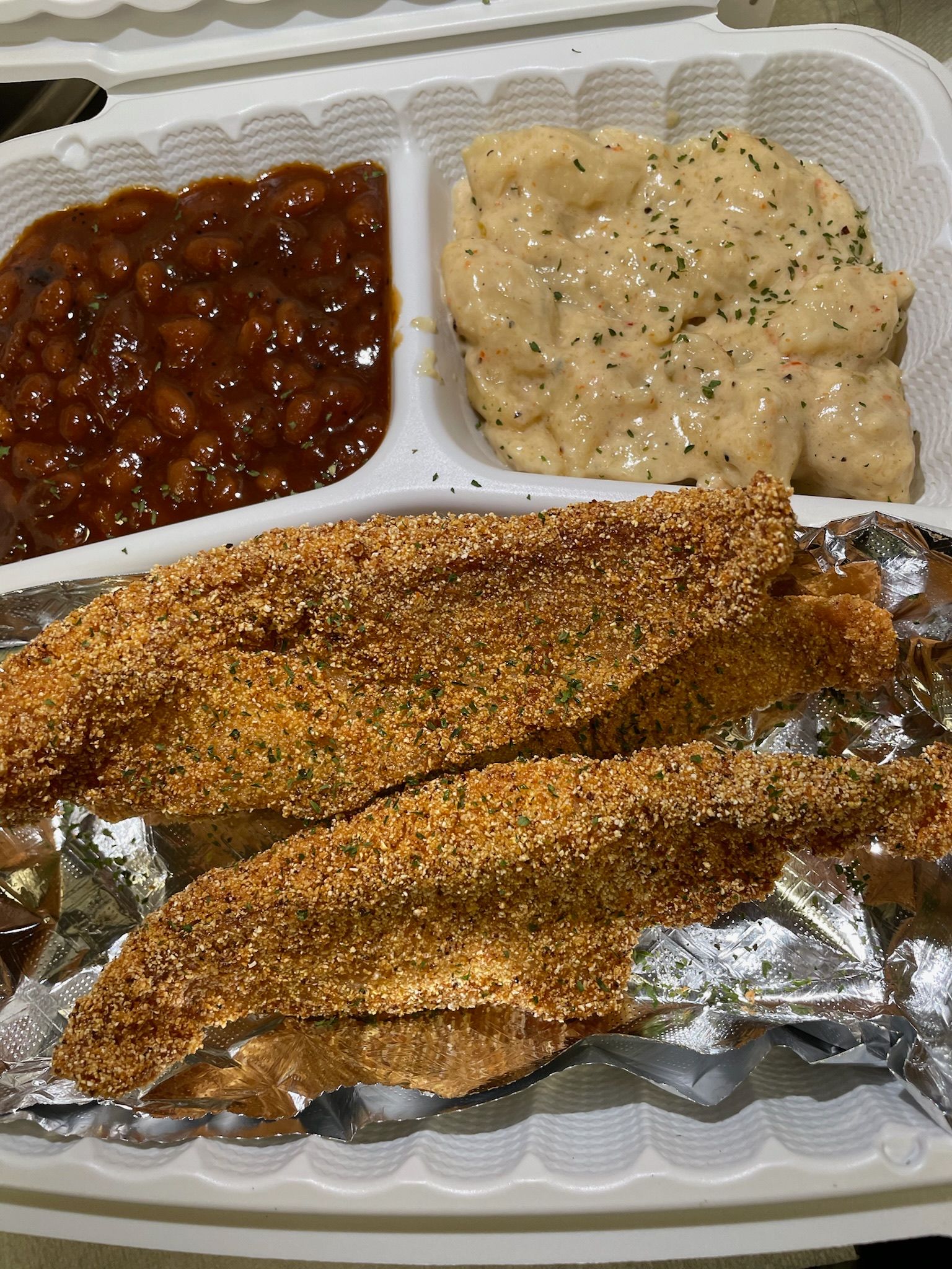 A plastic container filled with fried fish , macaroni and cheese , and baked beans.