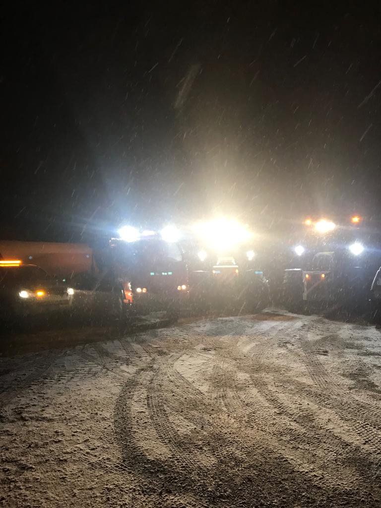 I fari abbaglianti di un camion illuminano di notte una strada buia e fangosa, con diversi veicoli in fila.