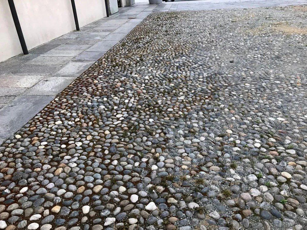 Sentiero ricoperto di ciottoli accanto a un marciapiede e un muro piastrellati.