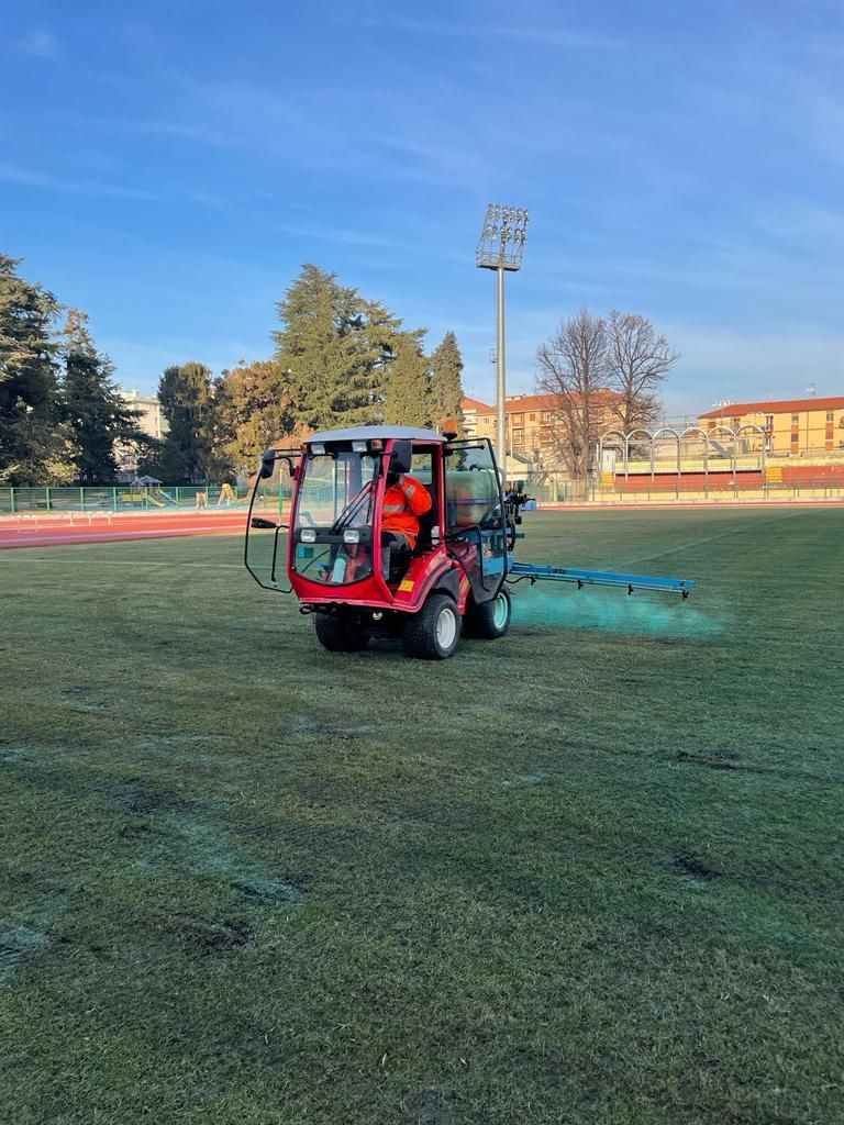 Un veicolo di manutenzione rosso spruzza acqua su un campo sportivo in erba in pieno giorno.