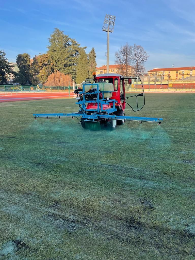 Un irroratore rosso su un campo sportivo, con la nebbia che si diffonde sull'erba all'alba.