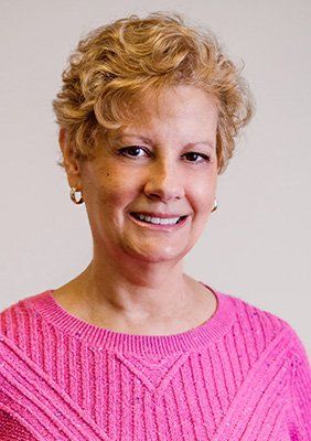 A woman wearing a pink sweater and earrings is smiling for the camera.