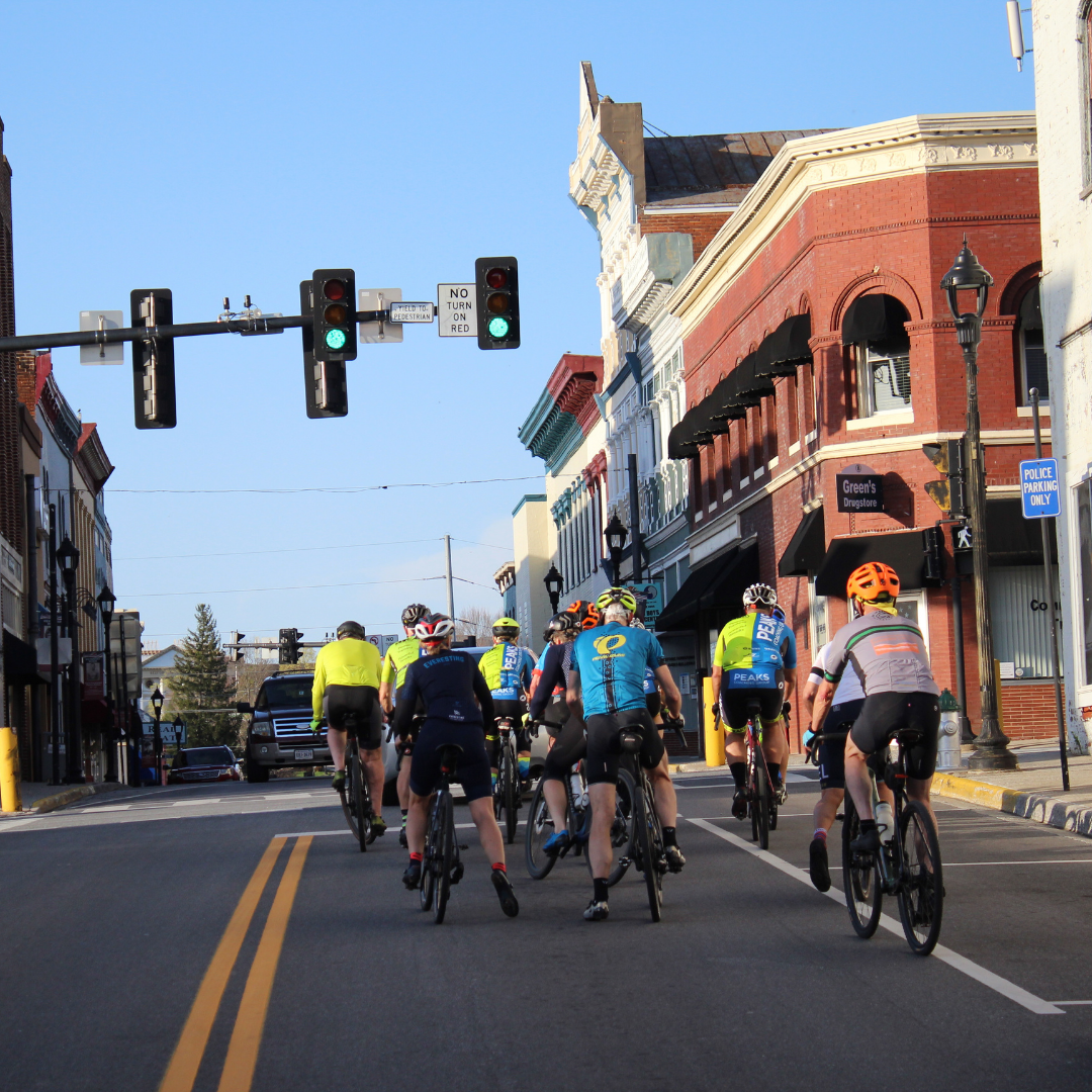 A group of people riding bikes down a street with a sign that says cals on it
