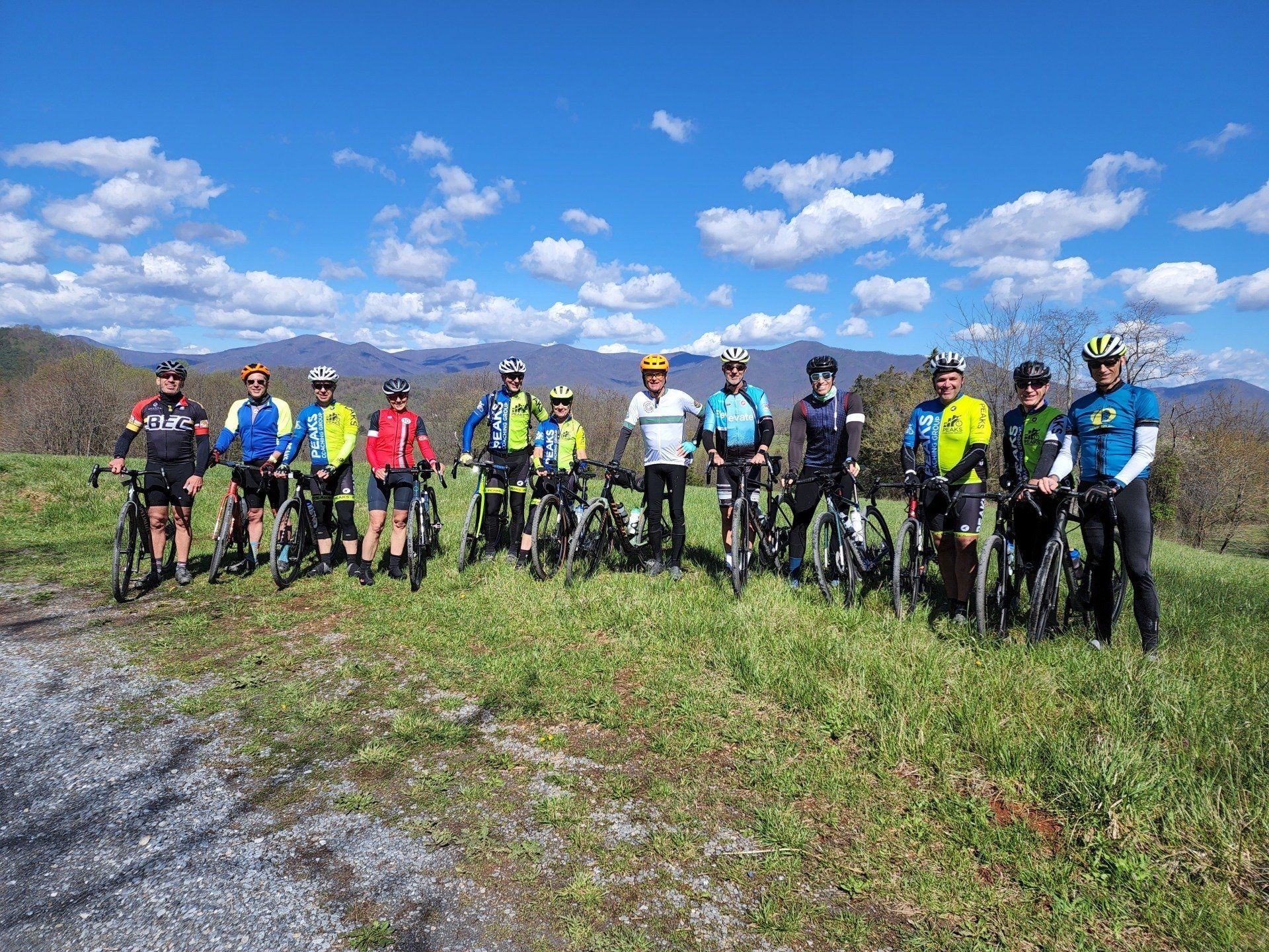 A group of cyclists are posing for a picture in a grassy field.