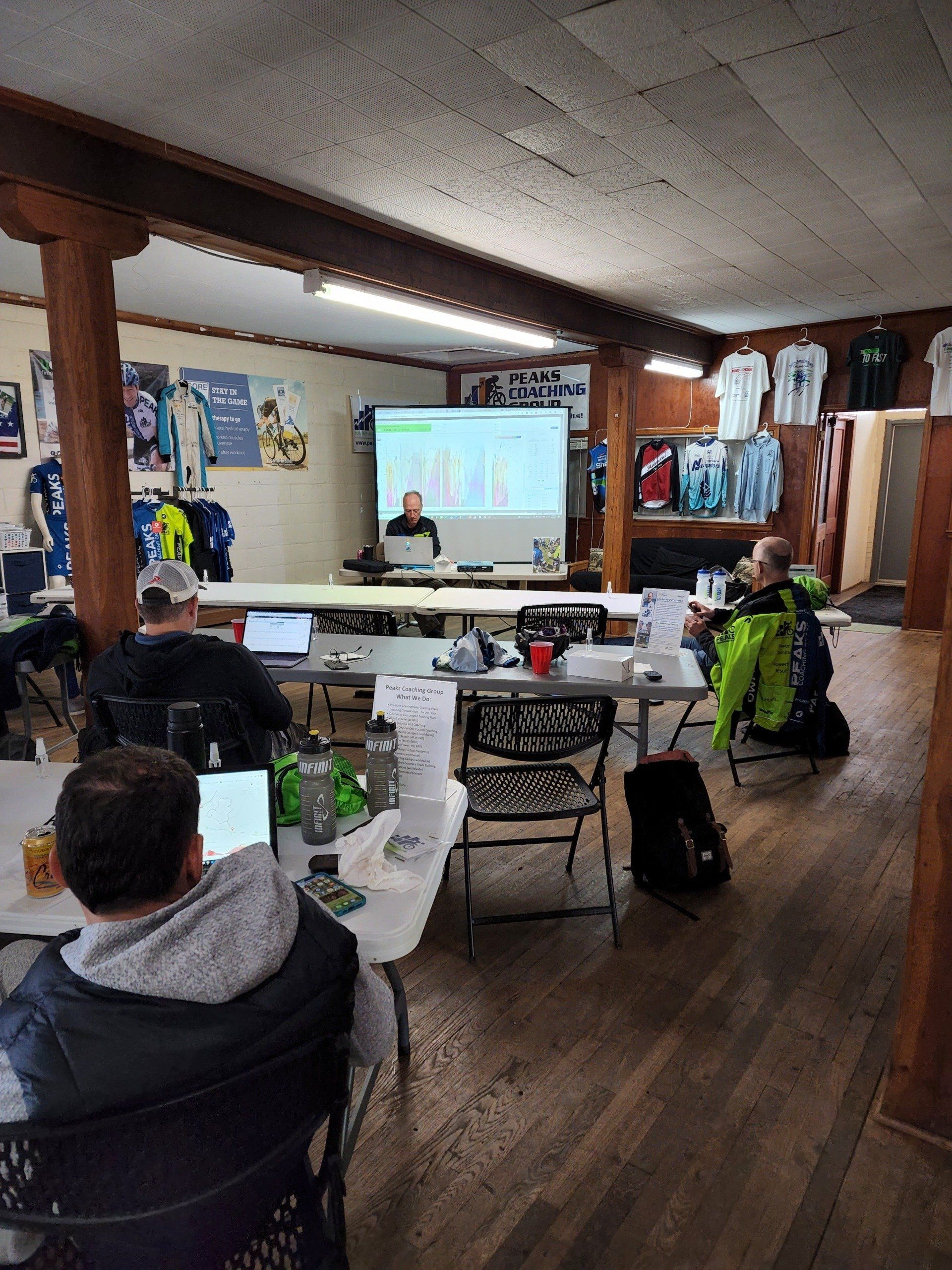 A group of people are sitting at tables in a room with a projector screen.
