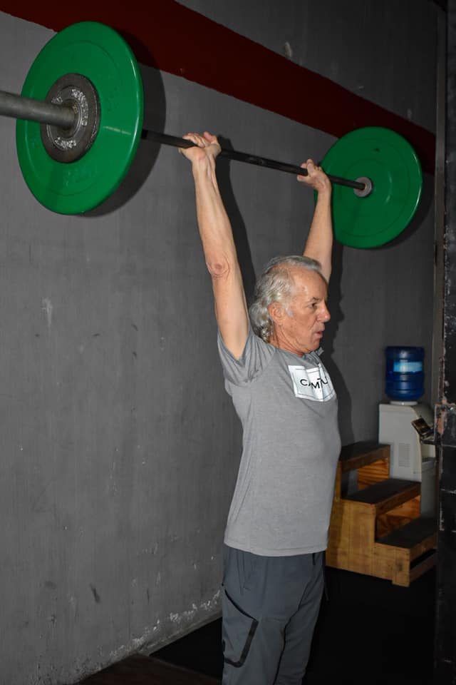 A man is lifting a barbell over his head in a gym.