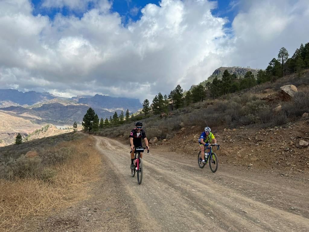 Two people are riding bicycles down a dirt road.