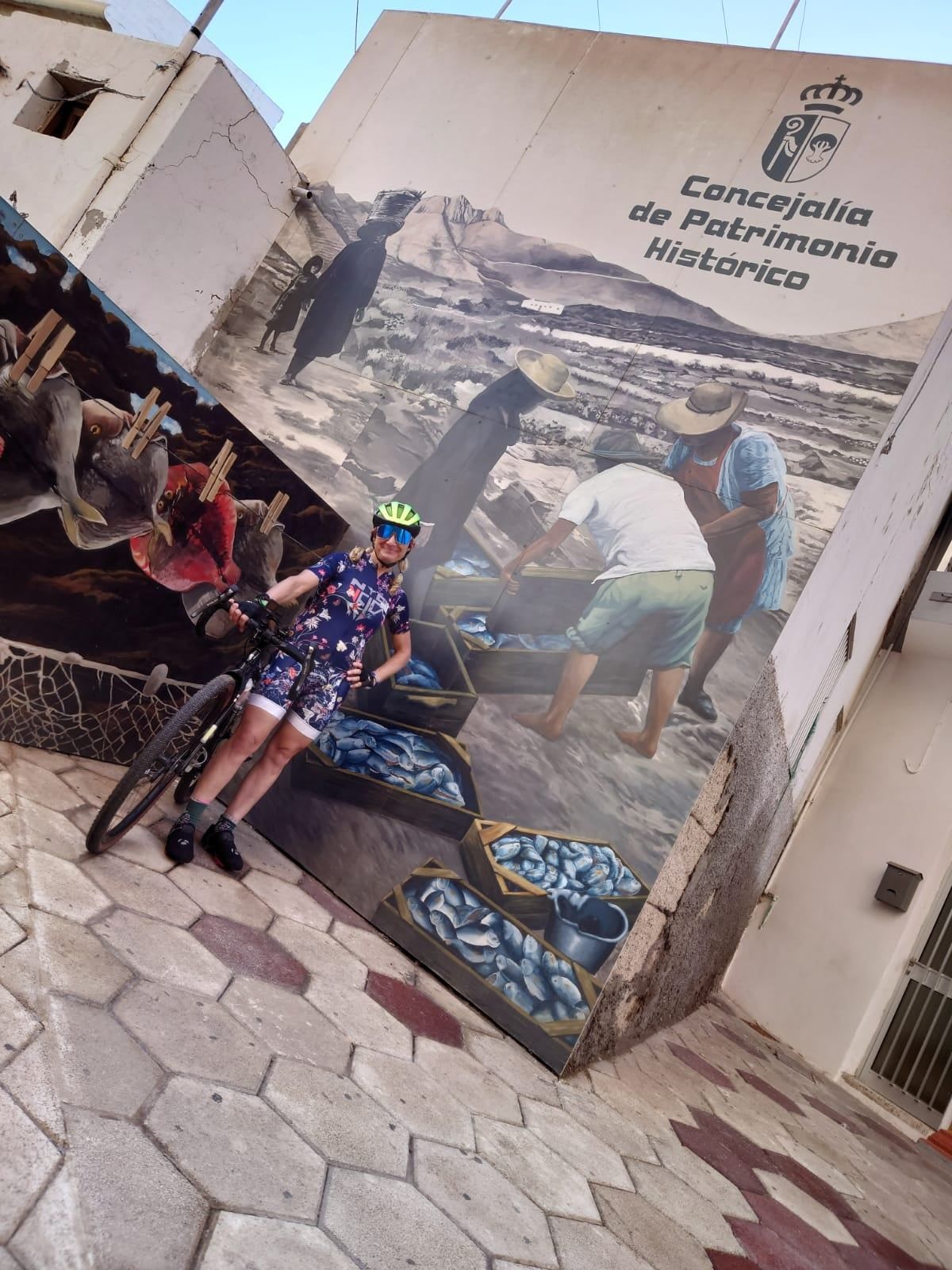 A woman is standing next to a bicycle in front of a large mural.