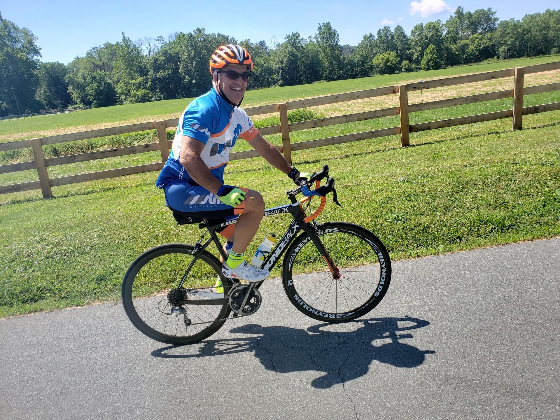 A man is riding a bike on a path next to a wooden fence.