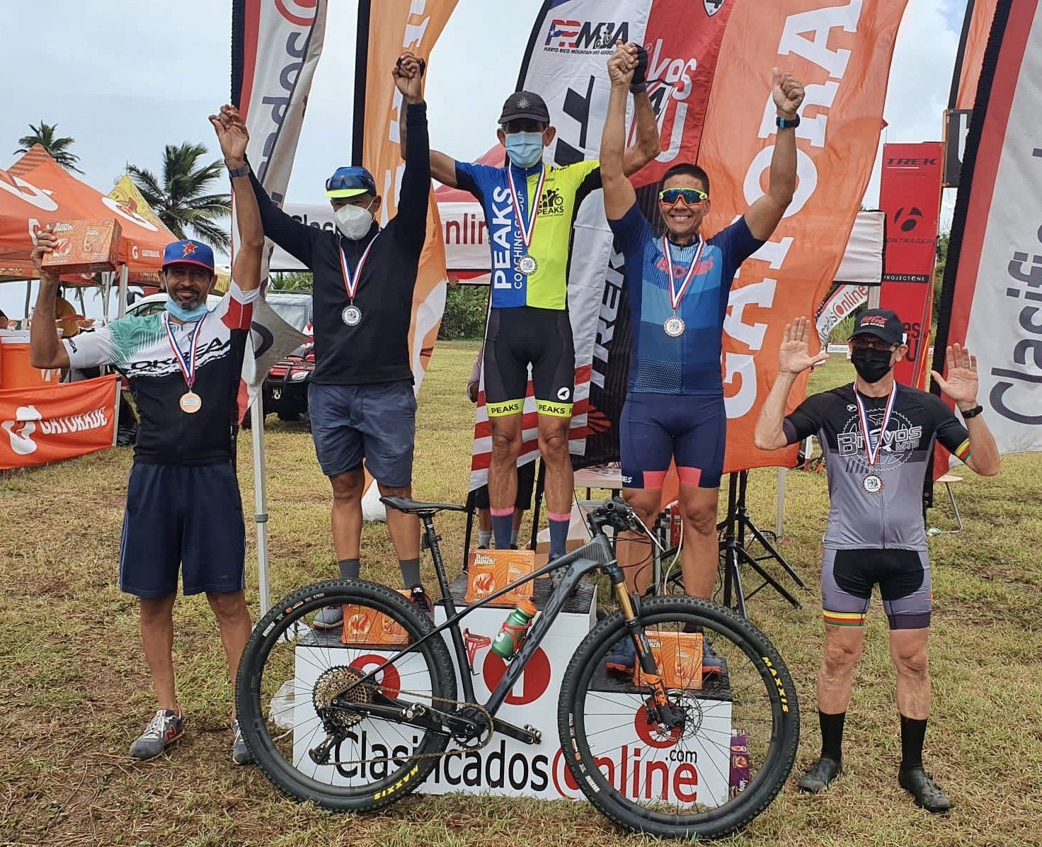 A group of men are standing on a podium with their arms in the air next to a bicycle.
