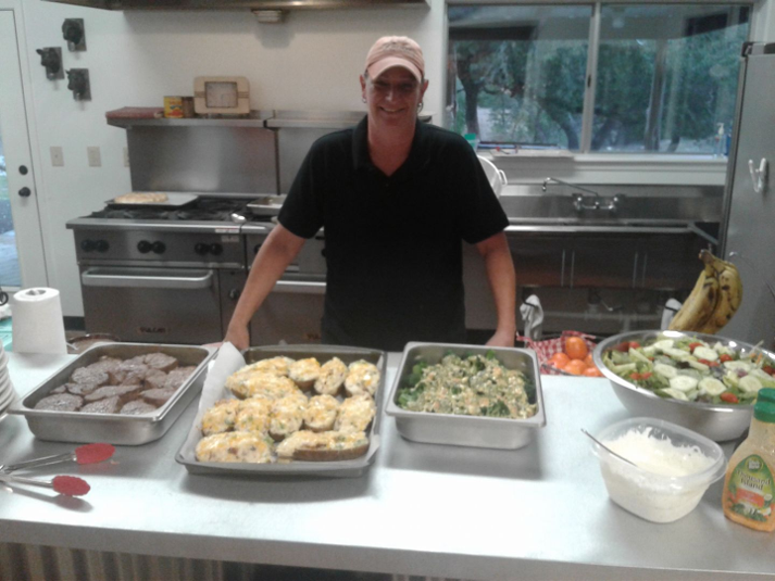 A man is standing in a kitchen with trays of food on the counter