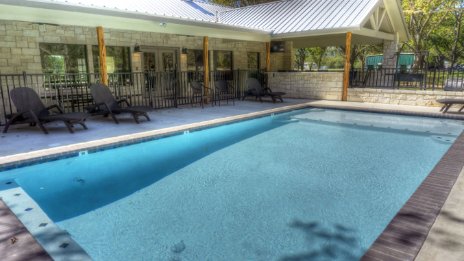 A large swimming pool is surrounded by chairs and a building.
